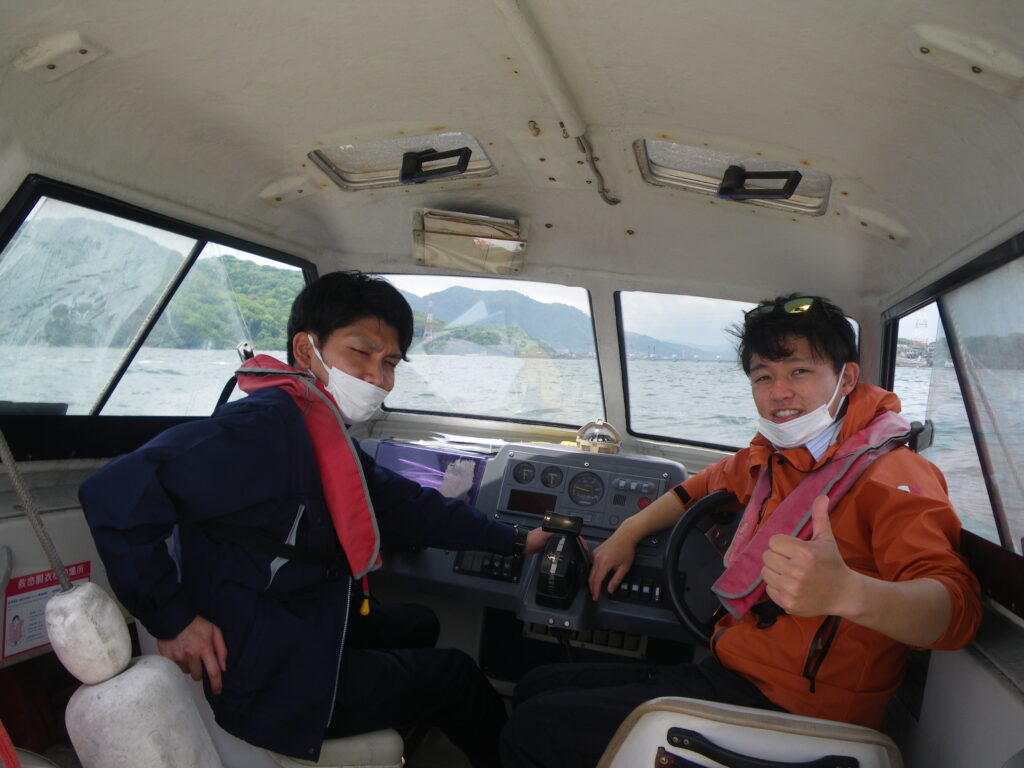 小型船舶の操縦席で親指を立てる教員と受講生
